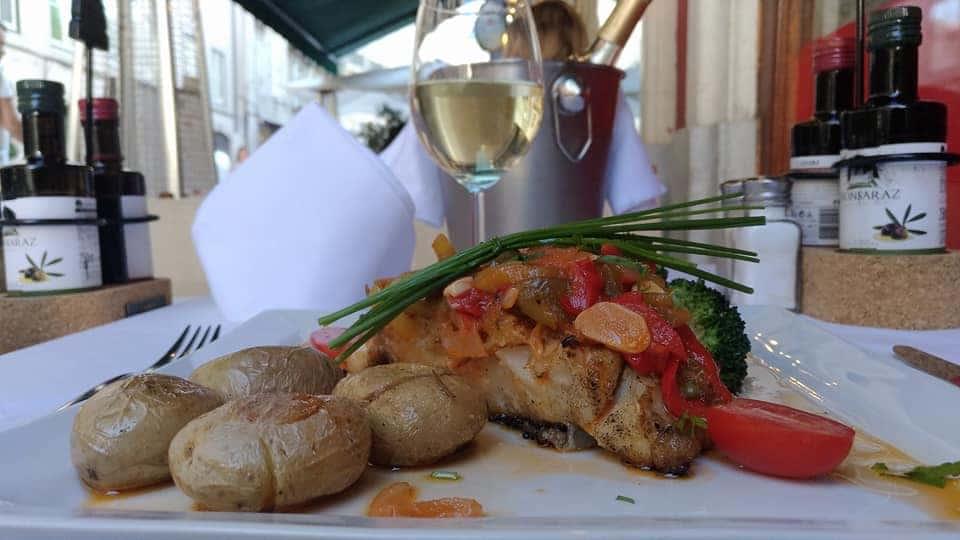 bacalhau assado com batatas e um copo de vinho branco