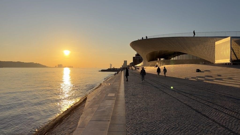 People walking along the river tagus with the maar museum in the background